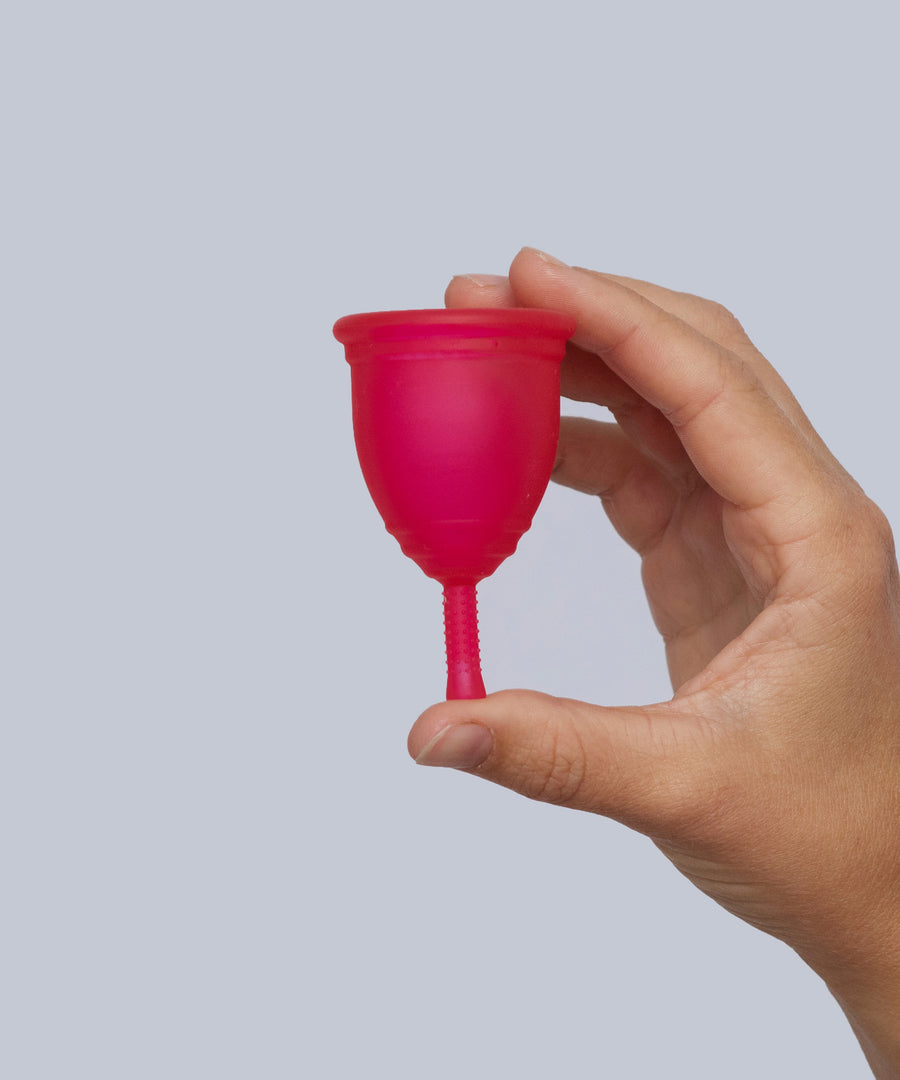 A person holding the Red Silicone, BPA free and latex free Ruby Cup in between their fingers, on a light grey background