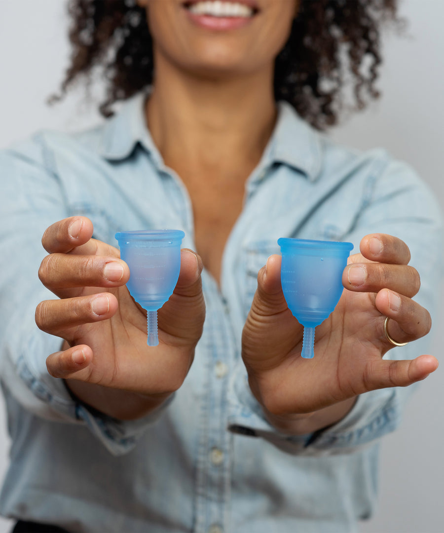 A person holding a large and small blue Silicone, BPA free and latex free Ruby Cup in between their fingers