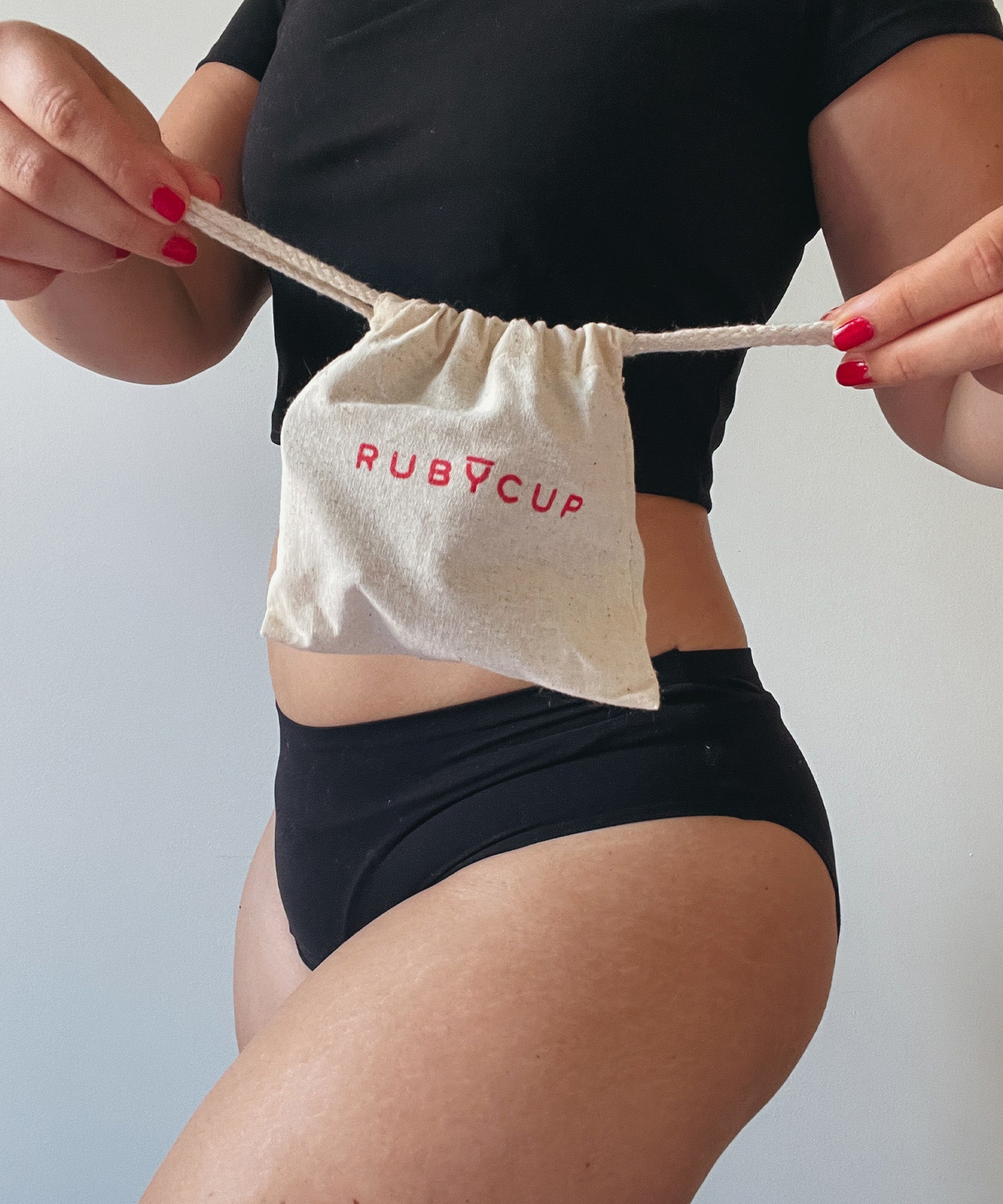 The drawstring storage bag which comes with the Ruby Cup menstrual cup, being held by a person who is pulling the drawstrings of the bag outwards