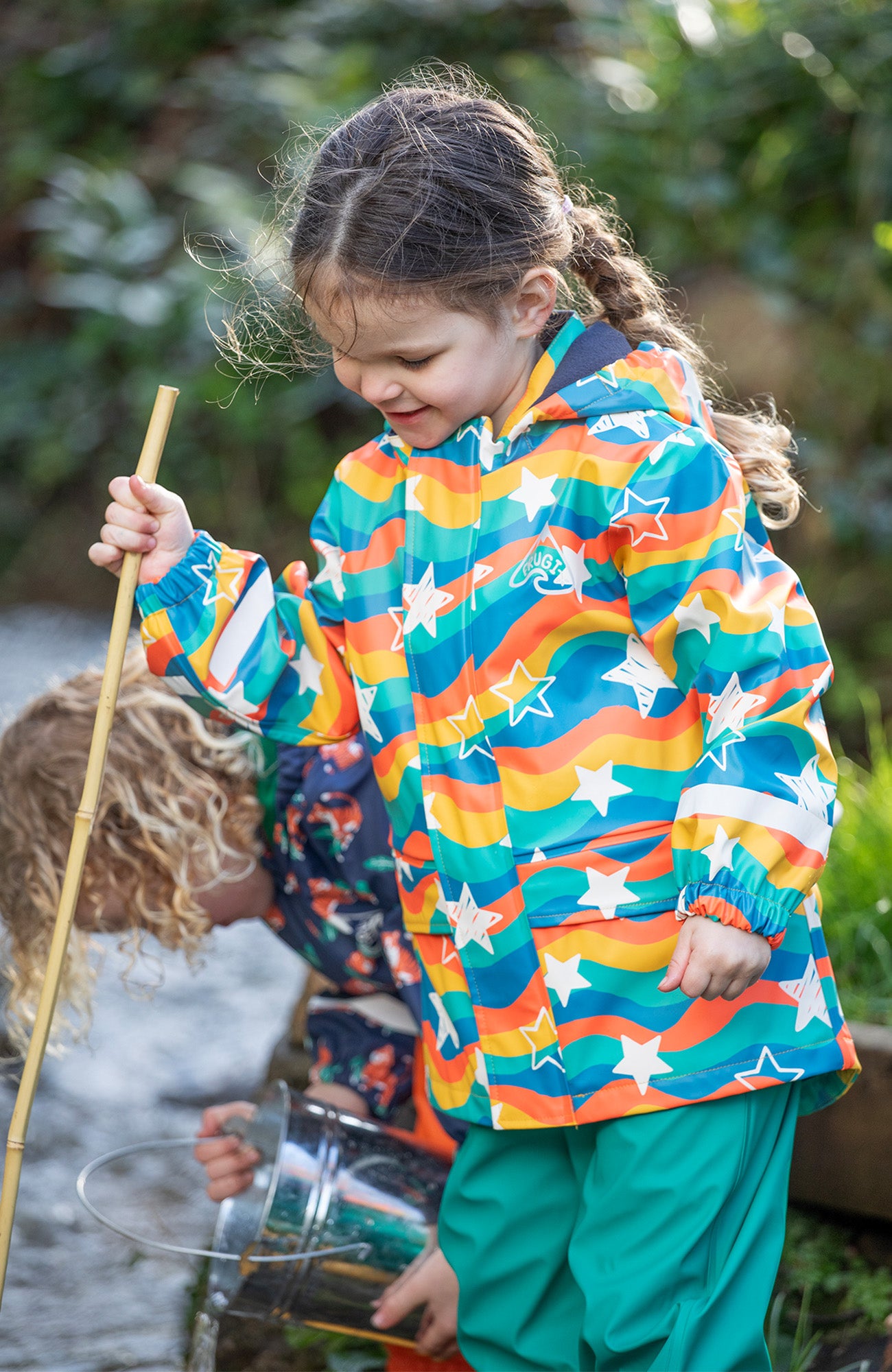 Children outdoors wearing Frugi waterproof colourful clothing, to represent mid season sale at babipur