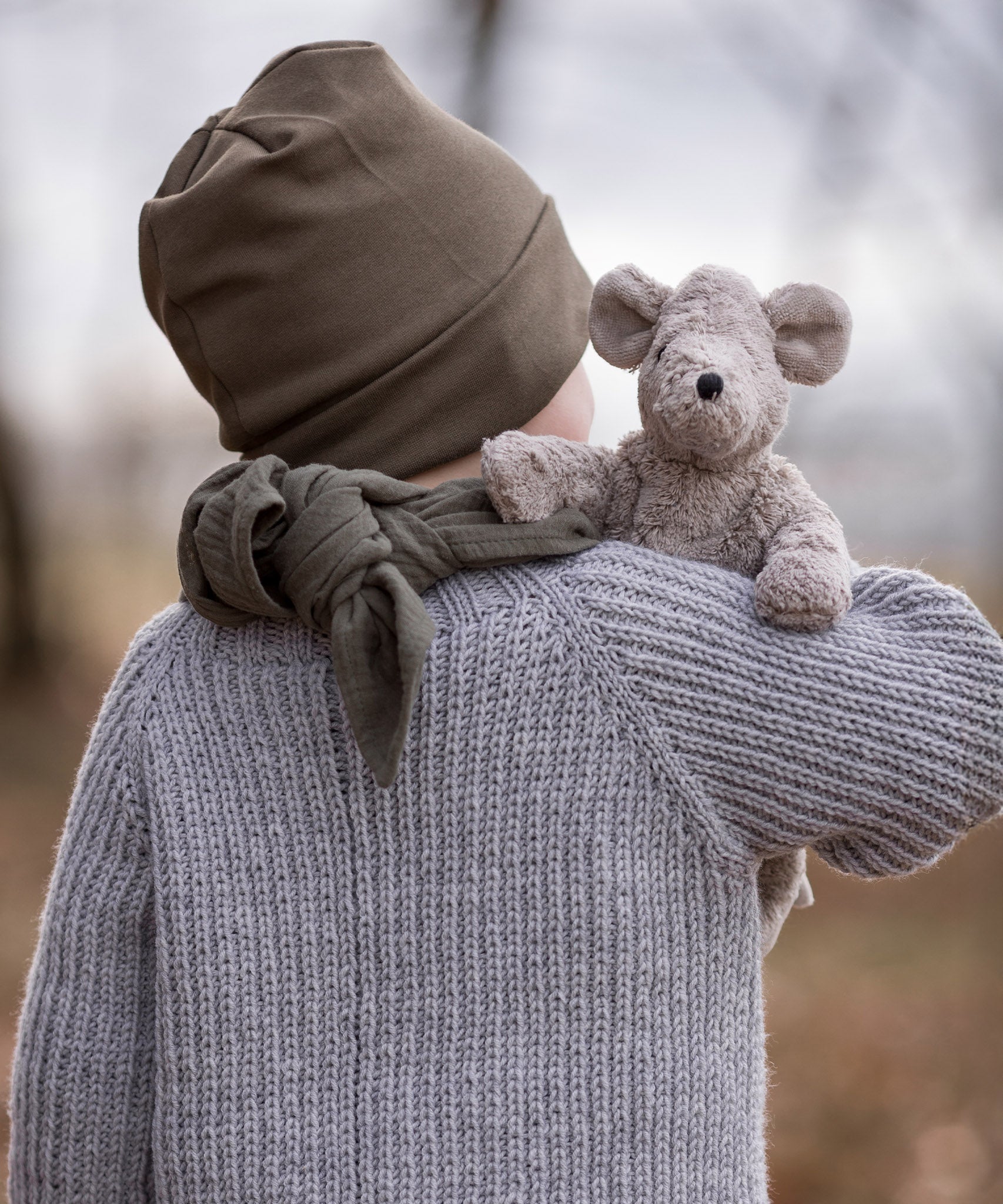 A child holding the Senger Baby Mouse in their arm, with the mouse showing over the child's right shoulder. The image is showing the back of the child