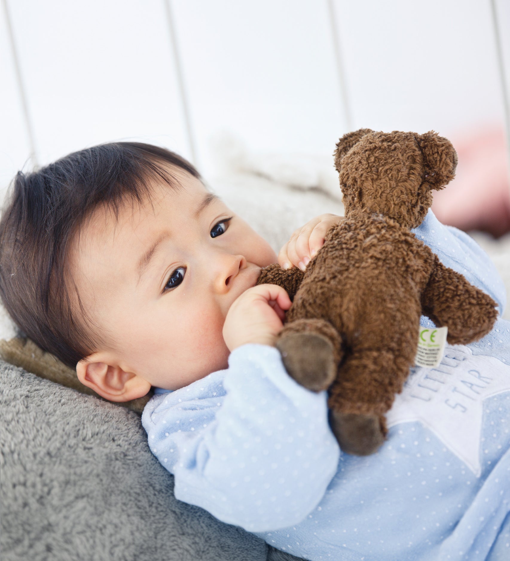 A child holding the arm of the Senger Baby Brown Bear next to their mouth