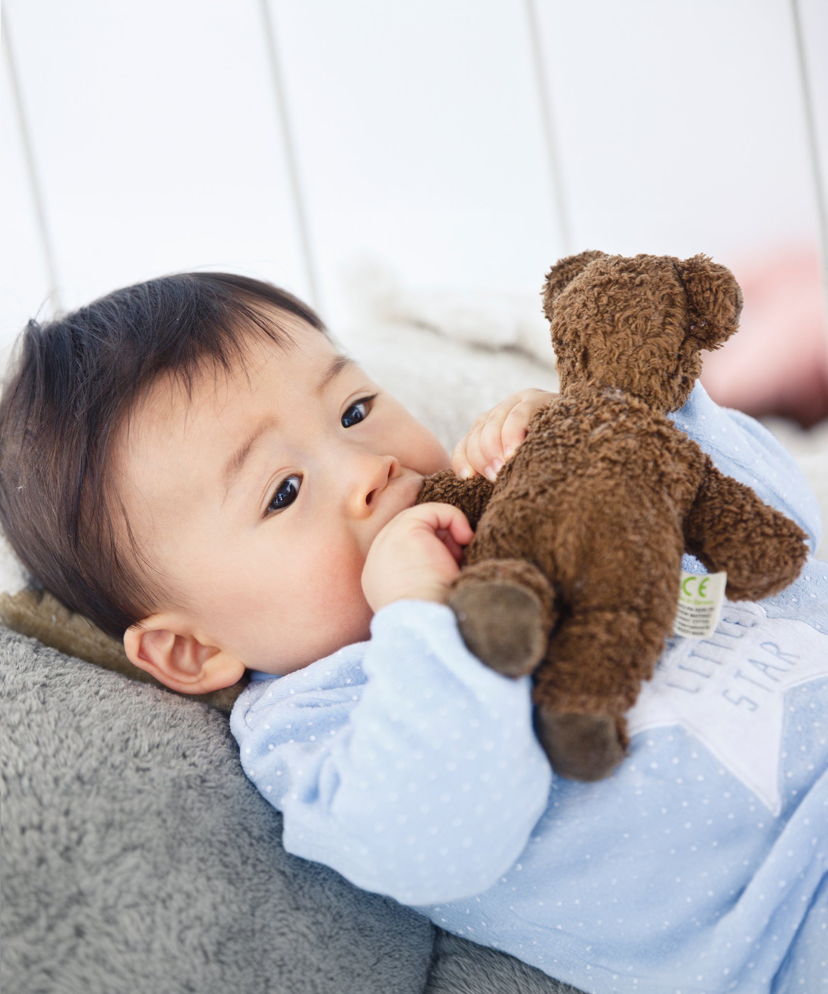 A child holding the arm of the Senger Baby Brown Bear next to their mouth