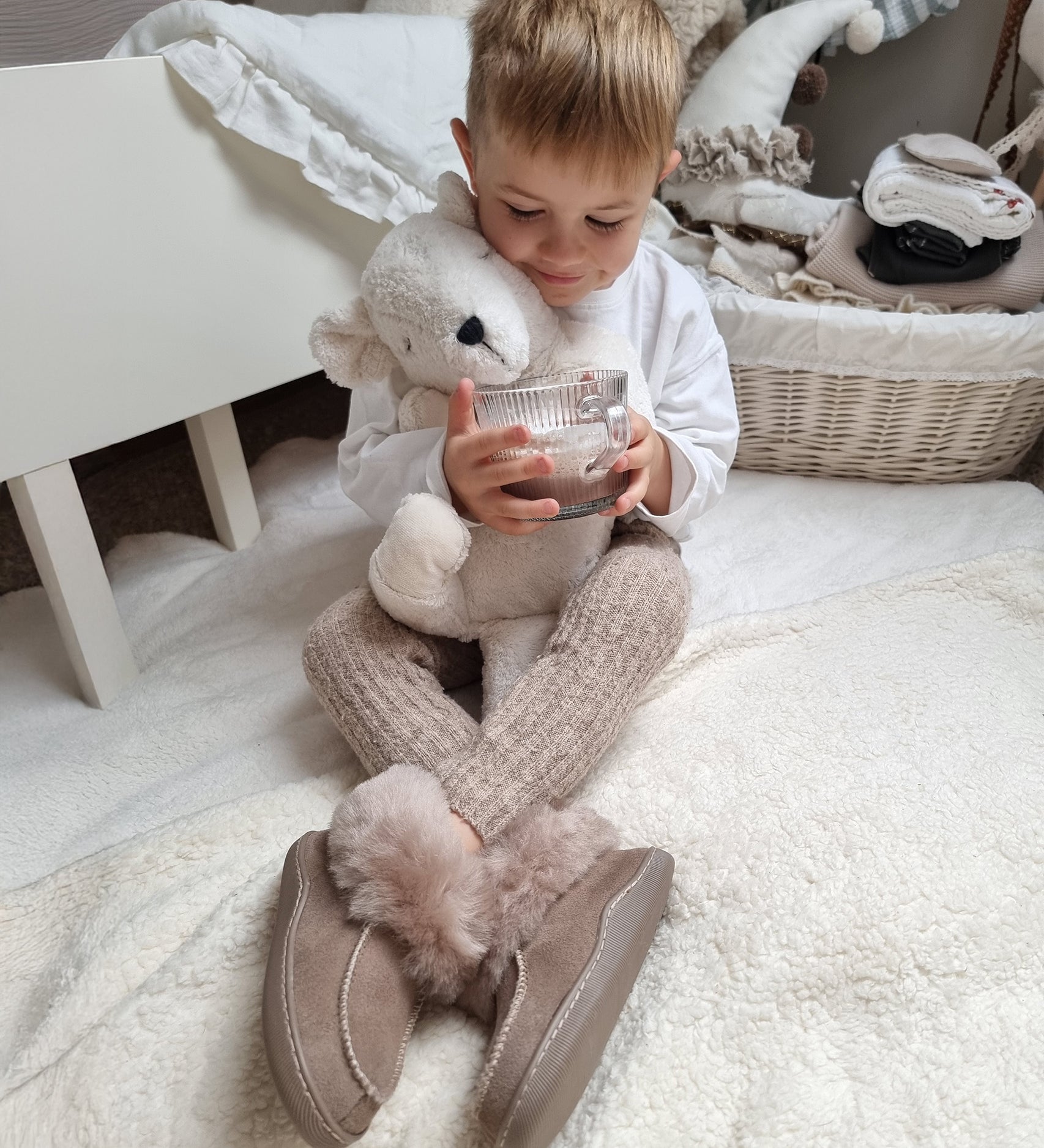 A child at on the floor in their room, holding the Senger Large Cuddly Polarbear and a cup of hot chocolate in their hand