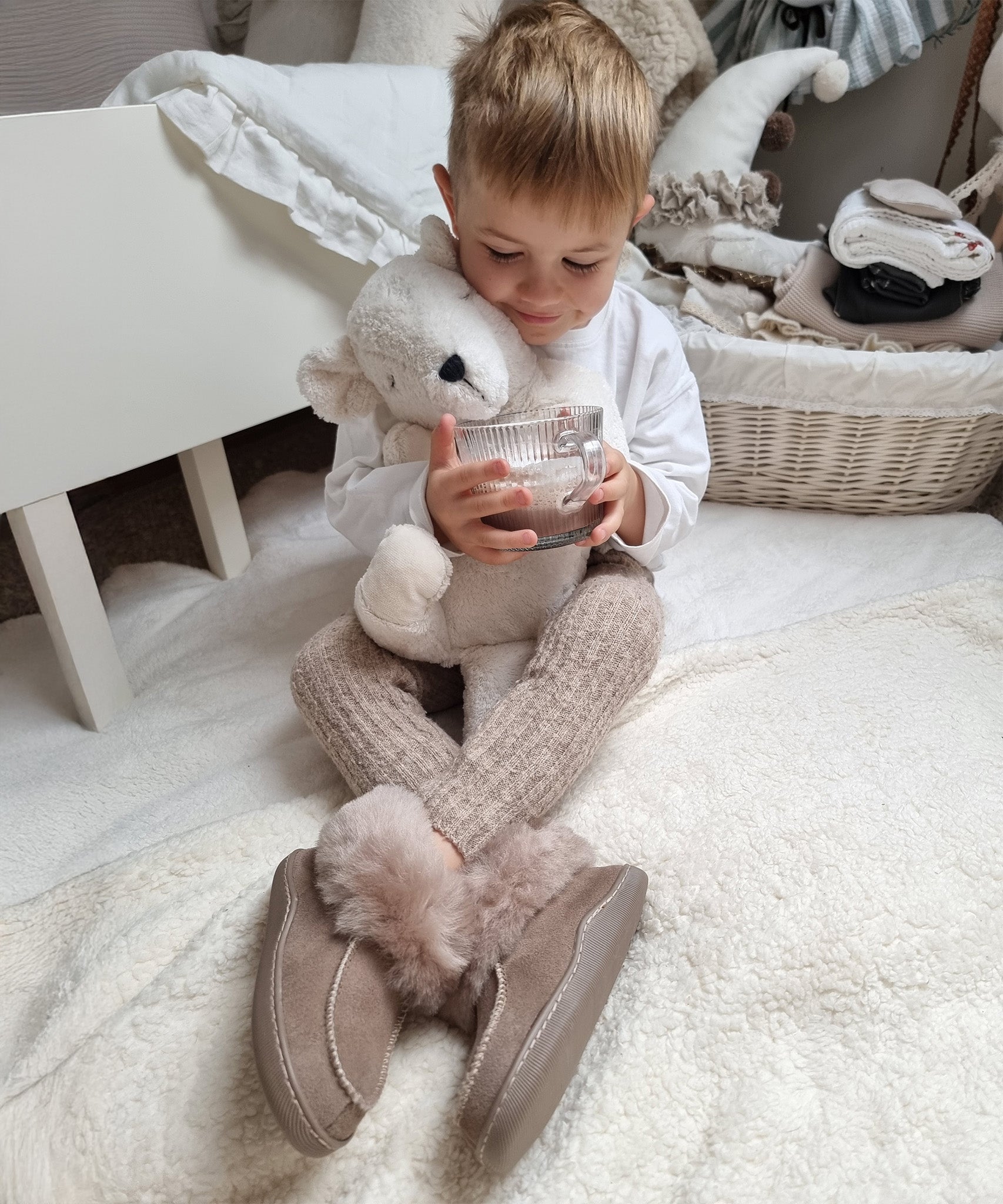 A child at on the floor in their room, holding the Senger Large Cuddly Polarbear and a cup of hot chocolate in their hand