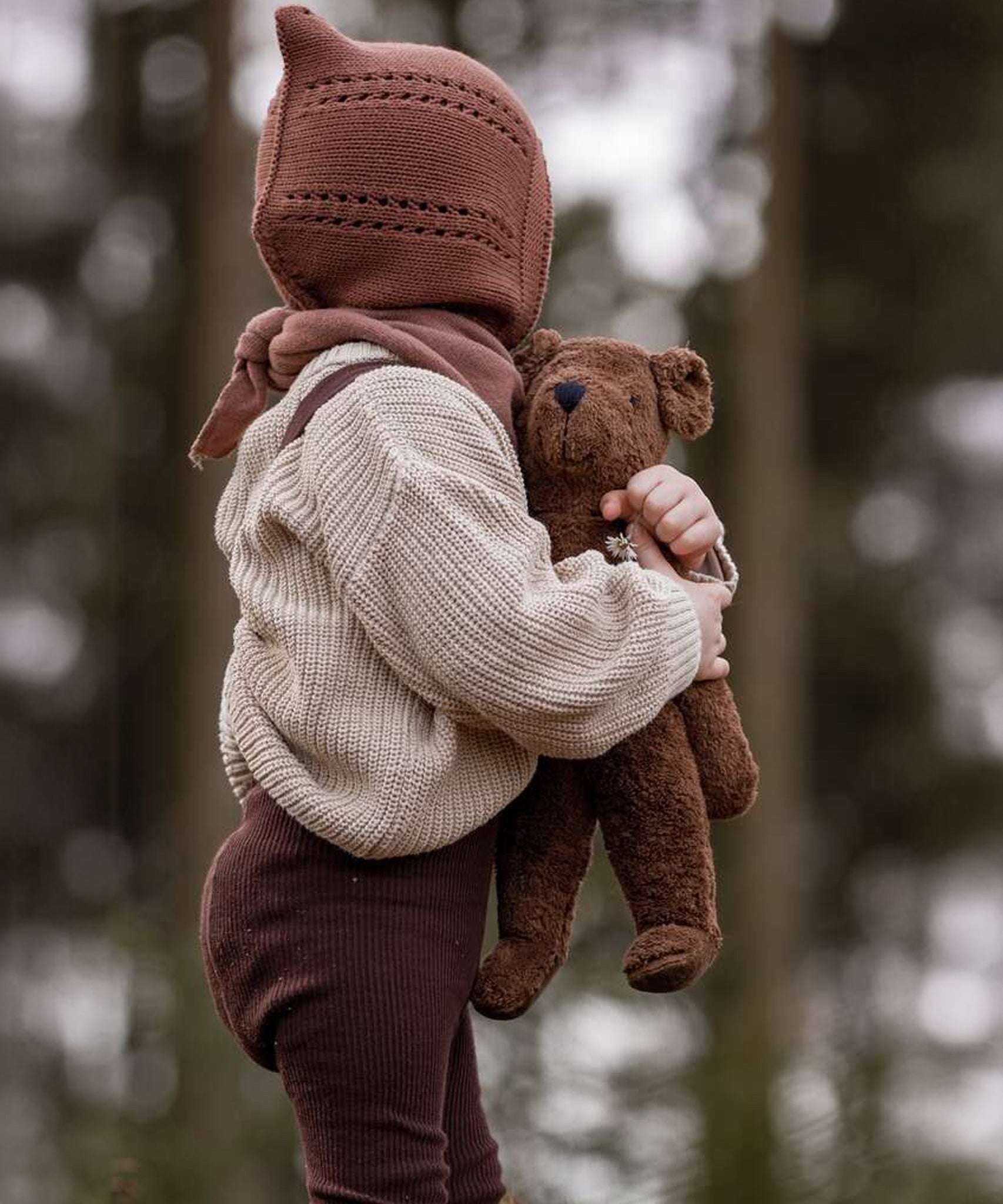 A child holding the Senger Small Floppy Brown Bear in their arms