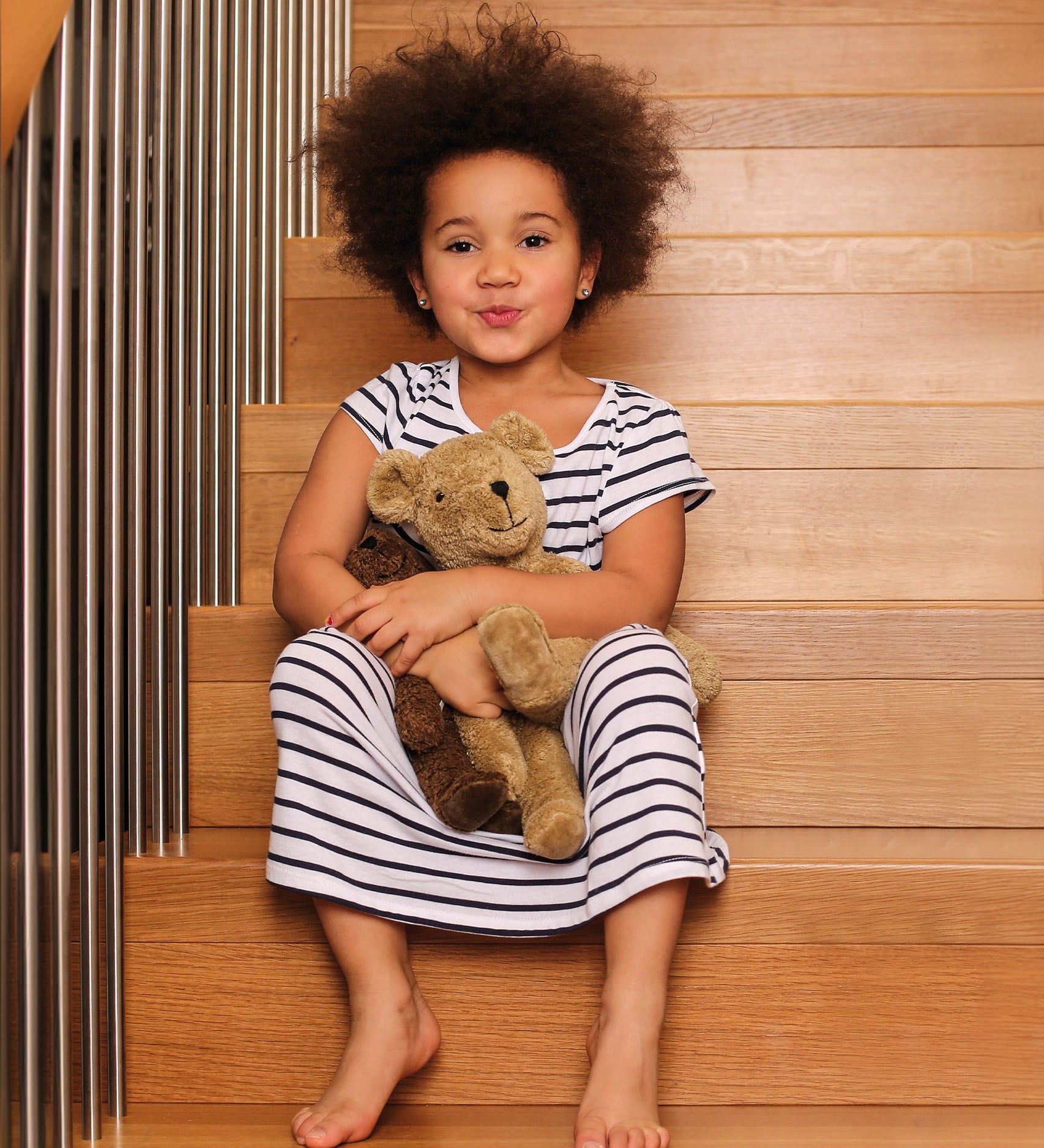 A child sat on wodden stairs, holding a Senger Large Floppy Beige Bear and small brown bear