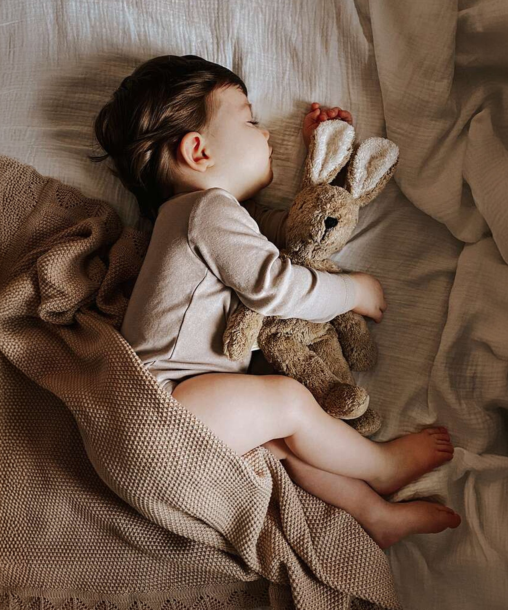 A child sleeping, cuddling the Senger Small Floppy Beige Rabbit