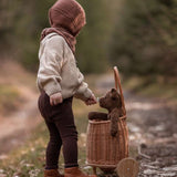 A child stood next to a bastet on wheels, with the Senger Small Floppy Brown Bear inside