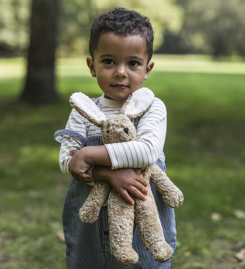 A child outside in a grassy field, holding the Senger Small Floppy Beige Rabbit in their arms