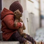 A child cuddling the Senger Small Floppy Brown Bear whilst sat on a step