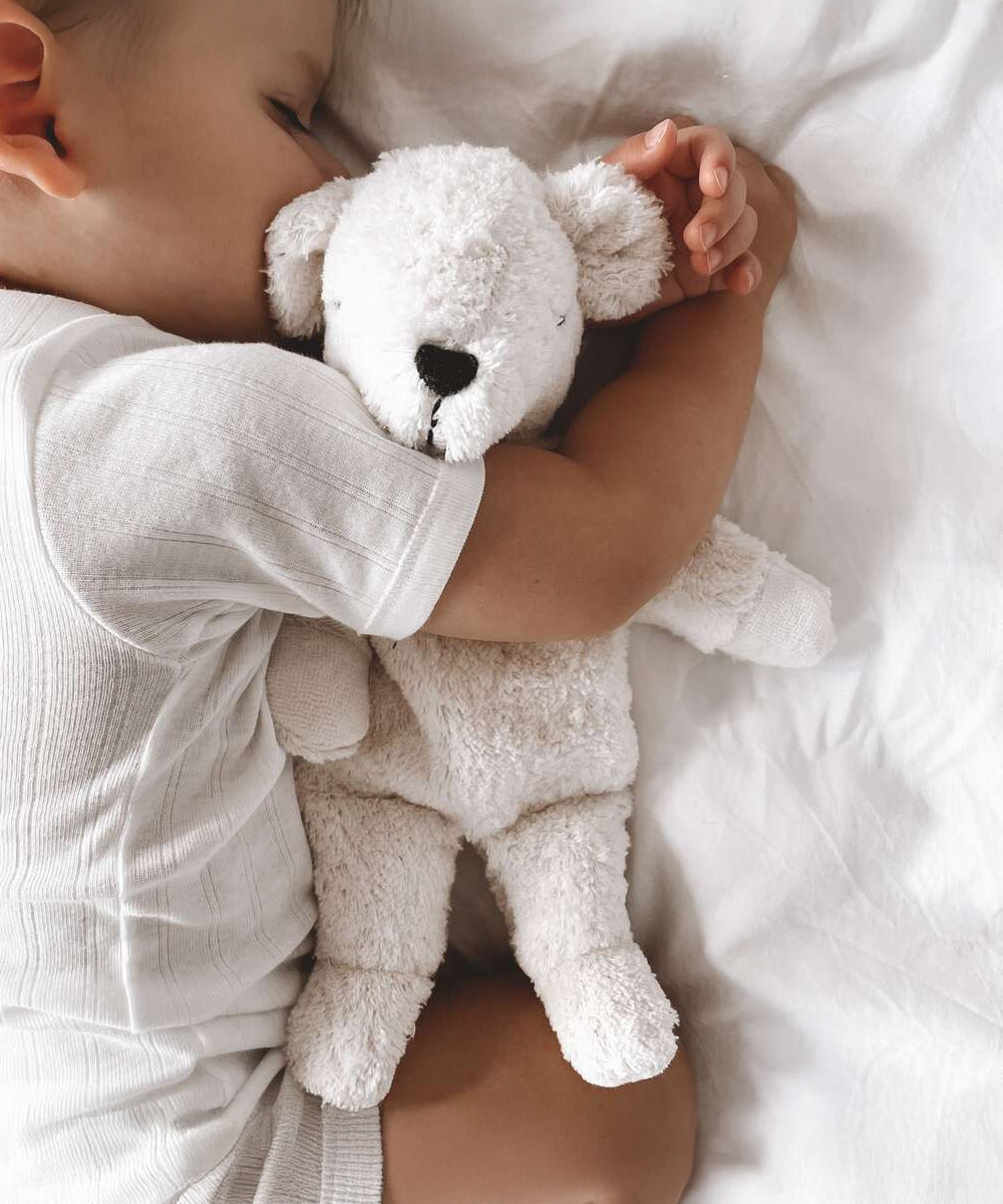 A sleeping baby cuddled up to the Senger Small Cuddly Polarbear