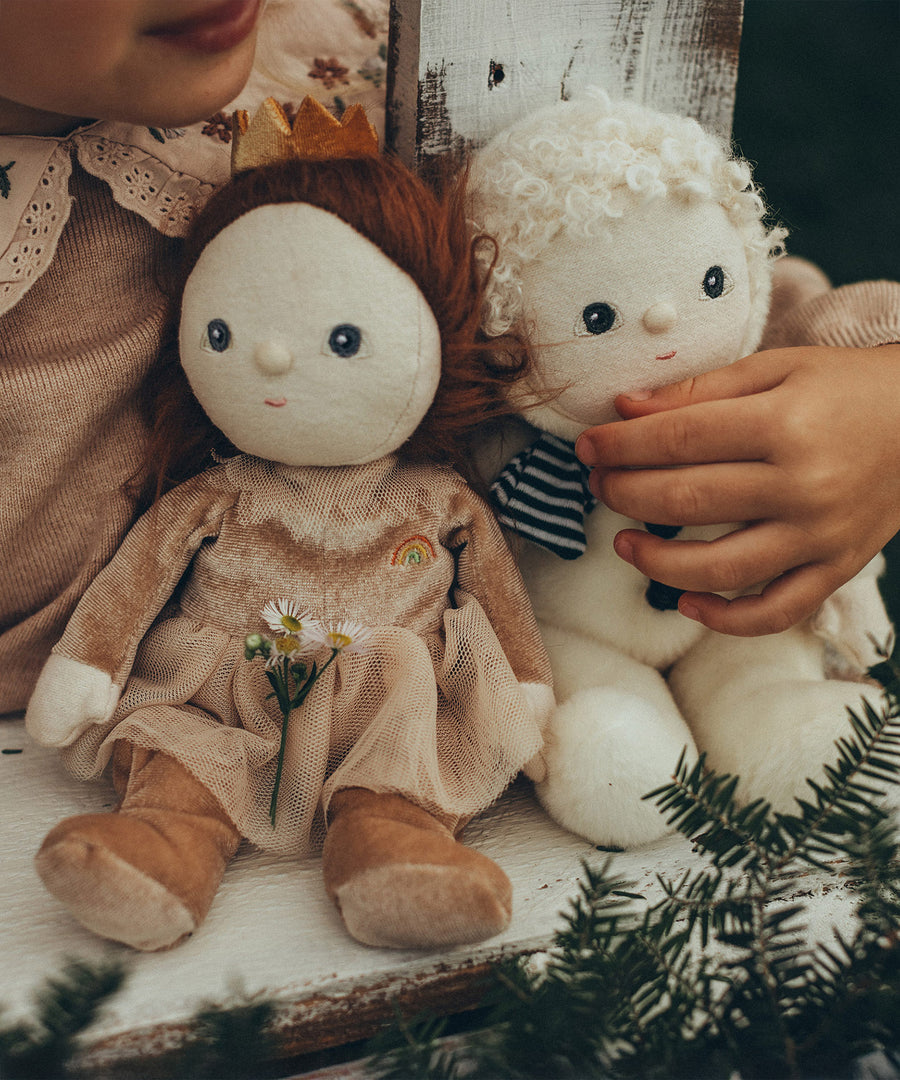 Sherry Sugarplum and Sidney Snowman Dinky Dinkum dolls sat next to each other, with a child holding onto Sidney and sat on a white wooden surface.