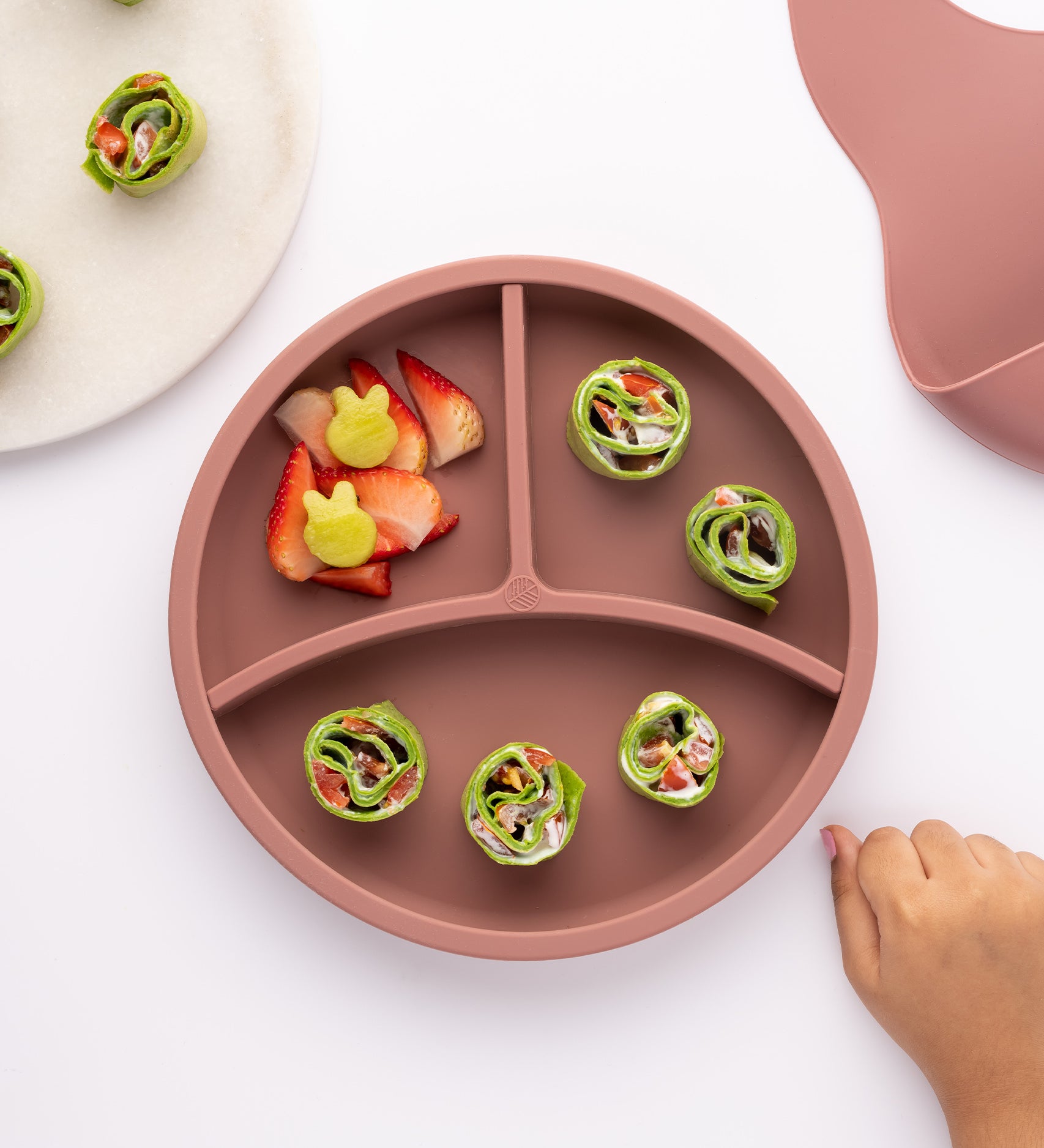 Eco Rascals Silicone Baby Plate in rose pink with removable divider, fresh fruit and green wraps.  