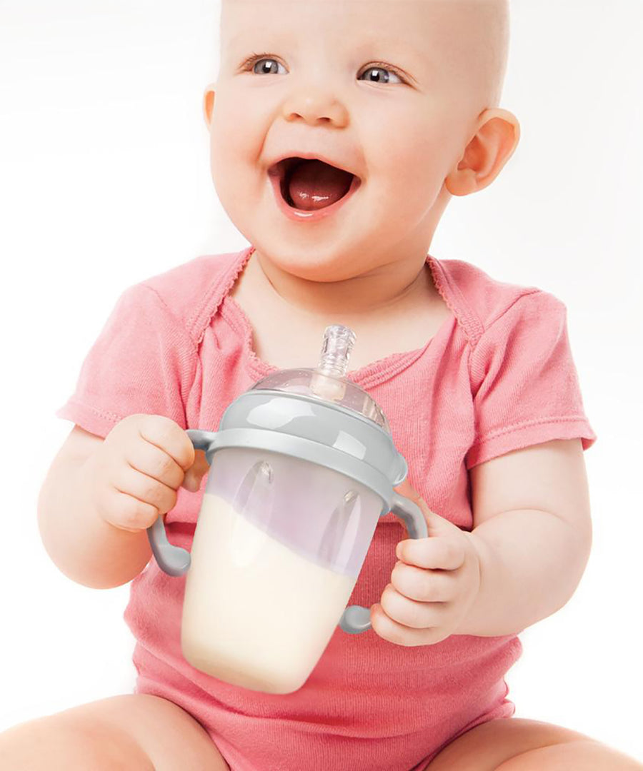 A baby smiling, and holding the Generation 3 Silicone Bottle Handle in their hands