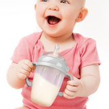 A baby smiling, and holding the Generation 3 Silicone Bottle Handle in their hands