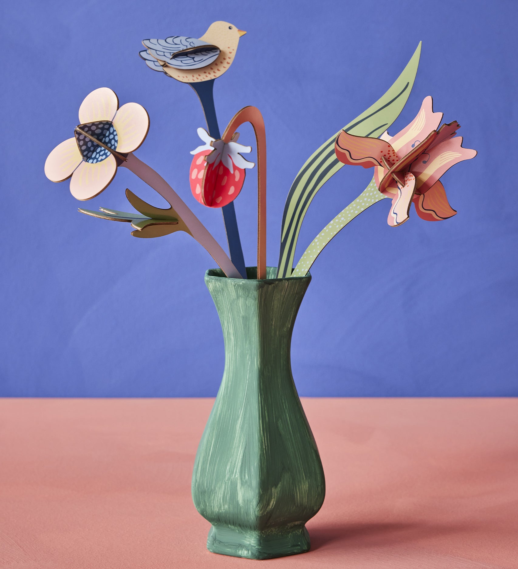 The Studio Roof Cardboard Bouquet - William Morris inside a green painted vase, on a blue/purple and peach background