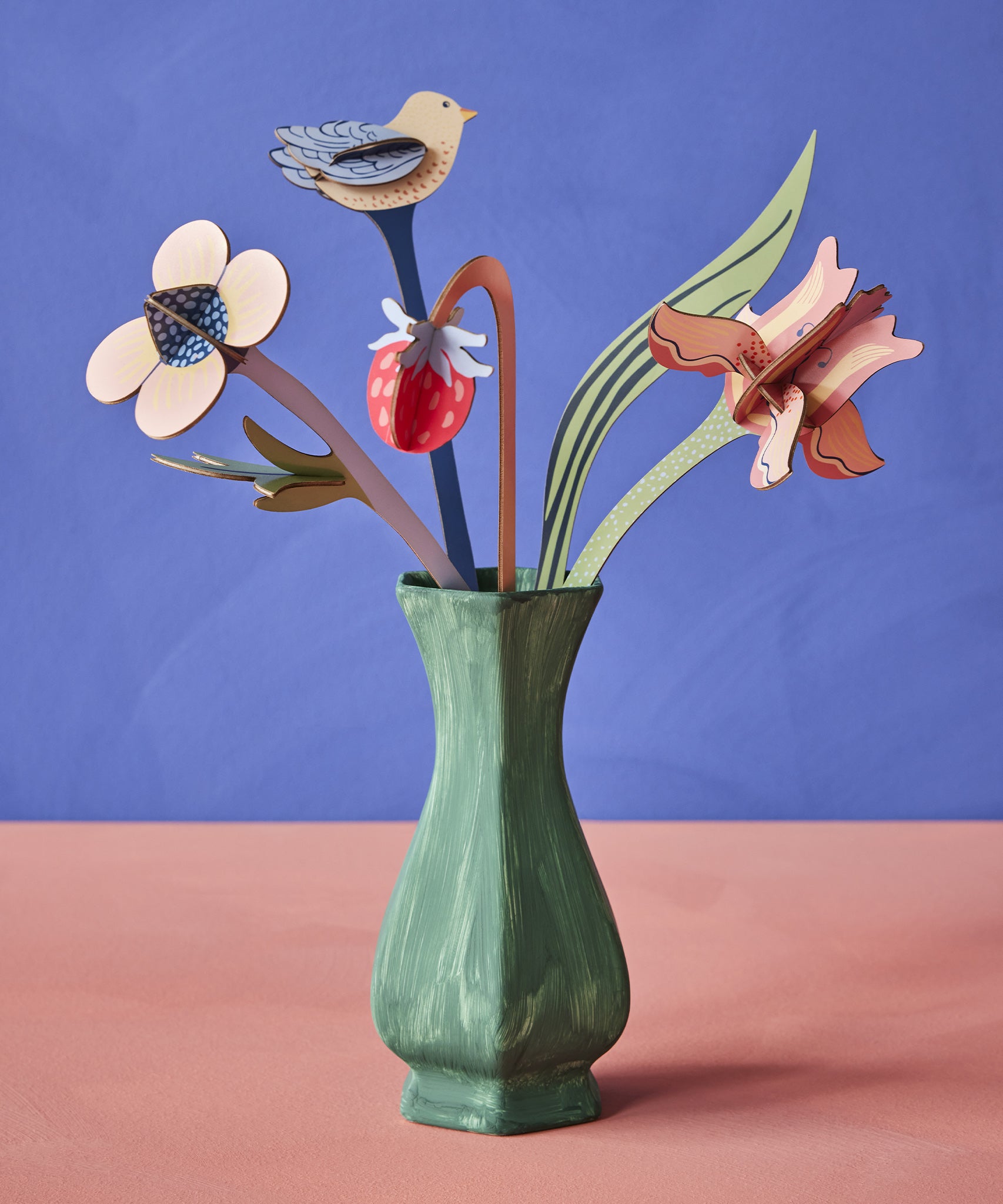 The Studio Roof Cardboard Bouquet - William Morris inside a green painted vase, on a blue/purple and peach background