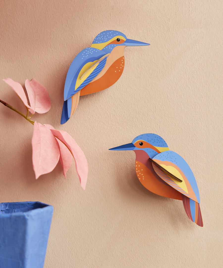 The Studio Roof Kingfishers are on a peach coloured wall, with a pink flower and blue vase in the bottom left corner of the photo