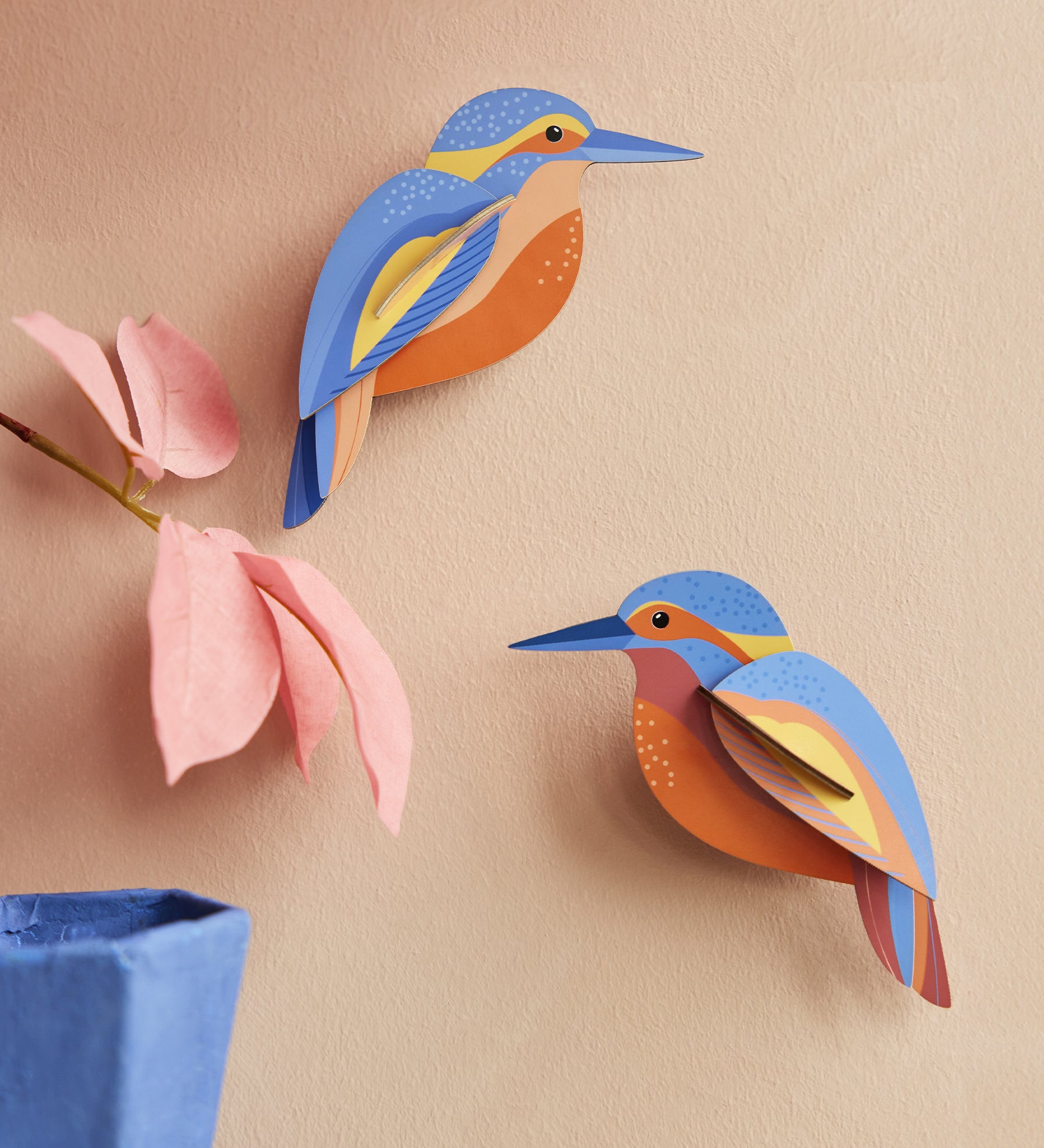 The Studio Roof Kingfishers are on a peach coloured wall, with a pink flower and blue vase in the bottom left corner of the photo