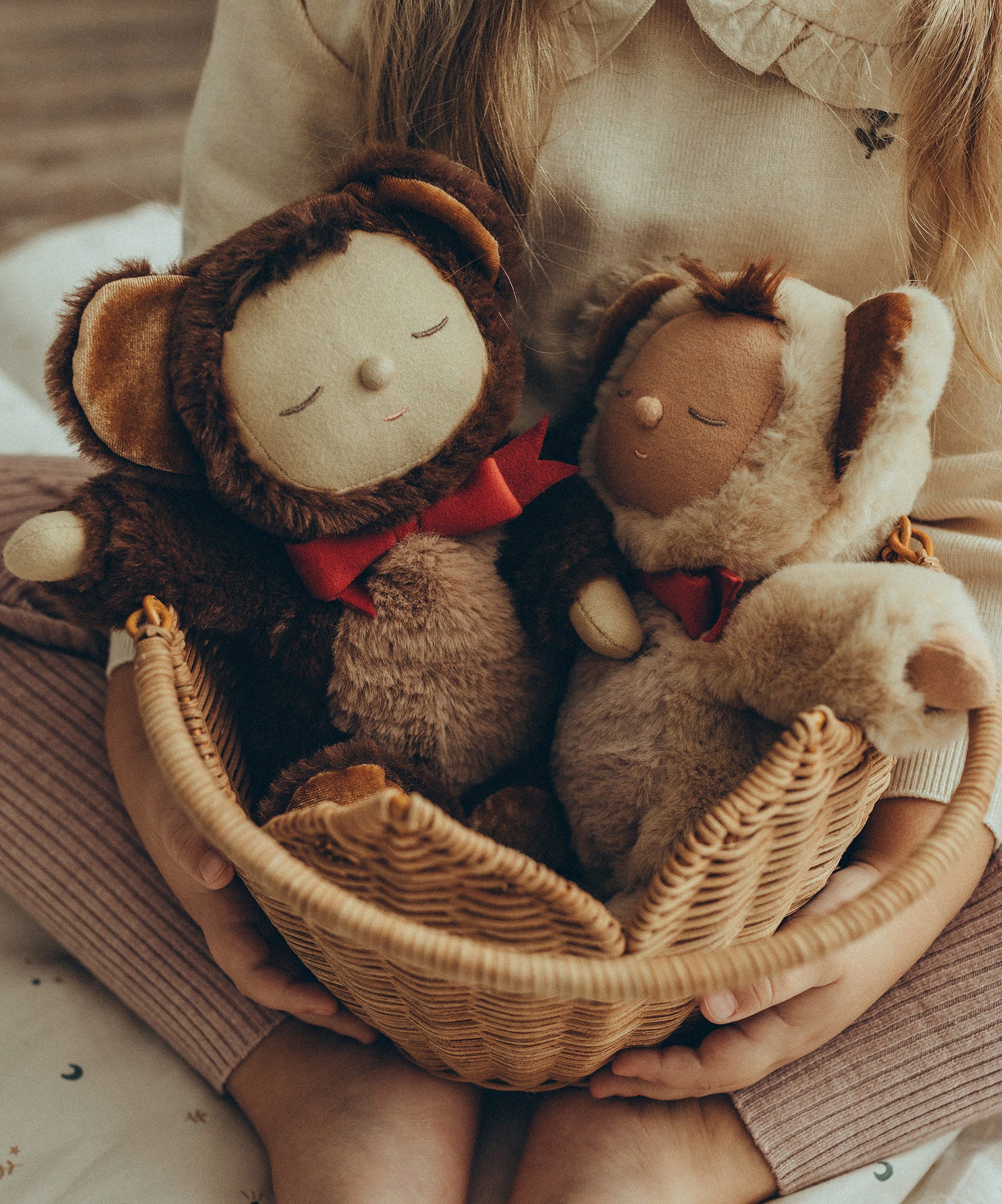 Olli Ella Cozy Dinkum Dolls Teddy Twiggy and Teddy Crumble together, sat in an Olli Ella Pionsettia Basket in natural, which is being held by a child