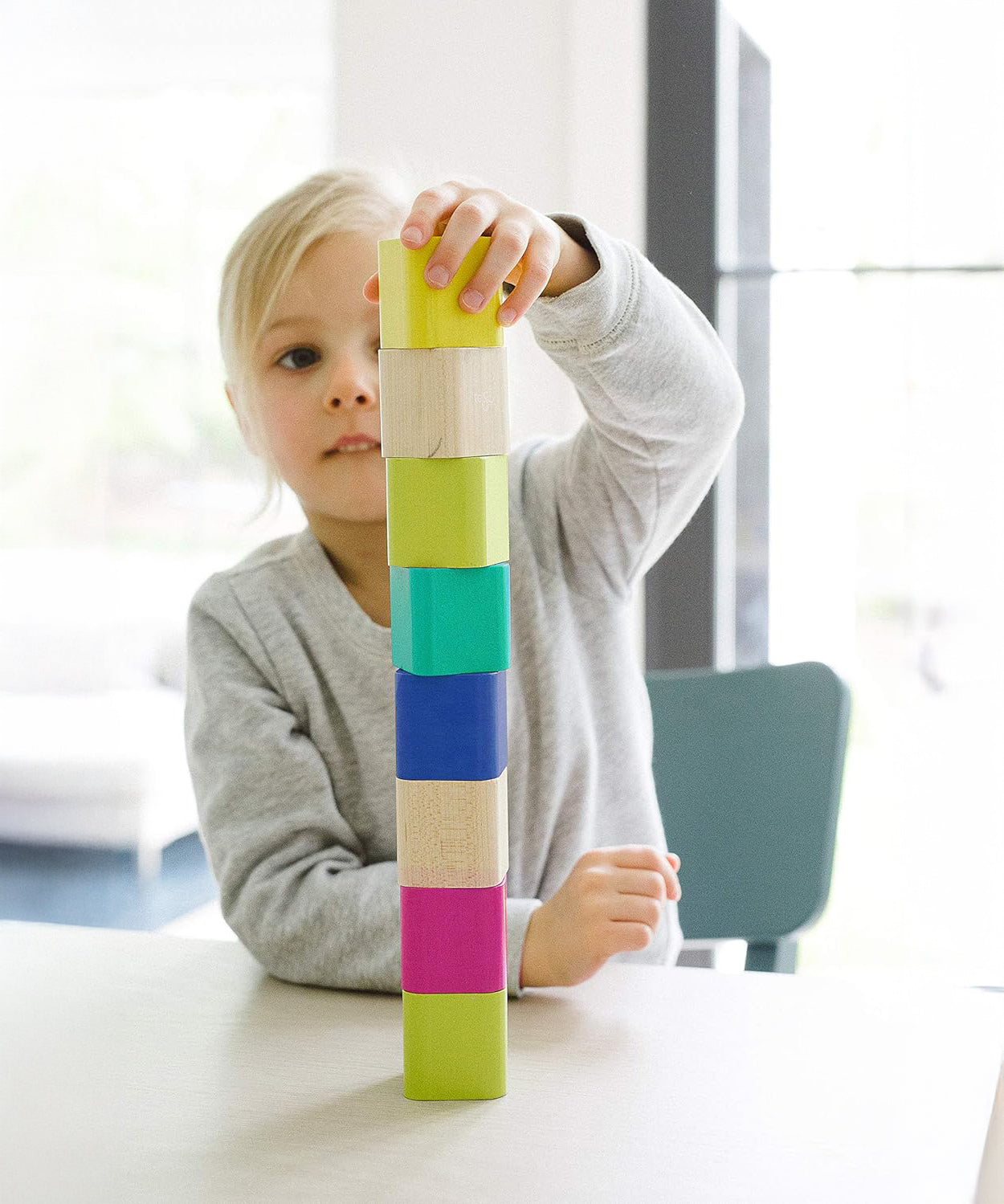 A child stacking the Tegu Magnetic Blocks on top of each other whilst sat at a white table