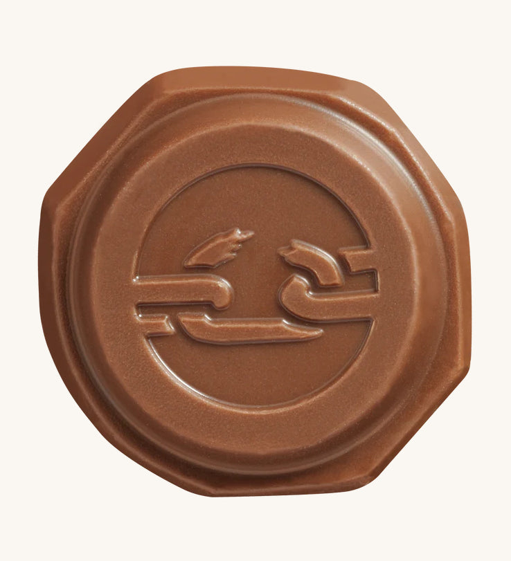 The front of the Tony's Chocolonely Tiny Mix chocolate button with the imprint of a broken chain on the front, to represent the breaking of slave labour. The image is on a cream background.