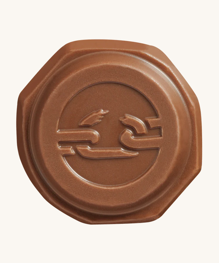 The front of the Tony's Chocolonely Tiny Mix chocolate button with the imprint of a broken chain on the front, to represent the breaking of slave labour. The image is on a cream background.