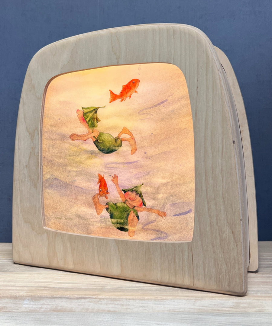 An illustration of two gnomes playing in water with goldfish from the Adventures Of Griswald Gnome Toverlux StoryLux Silhouette Sets, by Daniela Drescher. The illustration is inside a Magic Lamp which is stood on a table