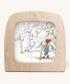 An illustration of a child skiing and meeting Jack Frost in a snowy wooded area from Ollie's Ski Trip Toverlux StoryLux Silhouette Sets, by Elsa Beskow. The illustration is inside a Magic Lamp on a cream background