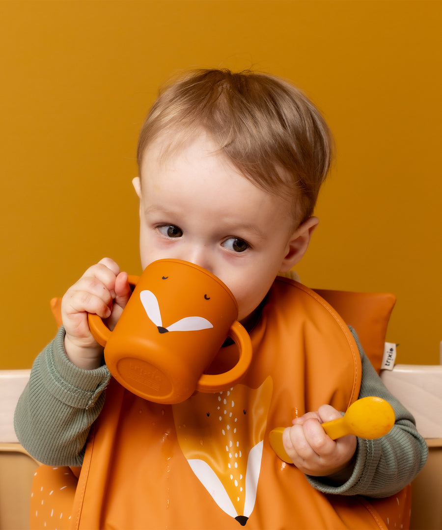 Baby drinking from the Trixie Animal Friends Silicone Sippy Cup, orange, Mr Fox. Wearing a matching bib. 