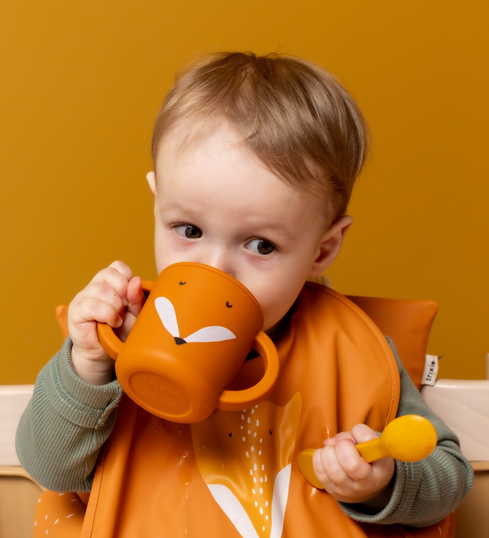 Baby drinking from the Trixie Animal Friends Silicone Sippy Cup, orange, Mr Fox. Wearing a matching bib. 