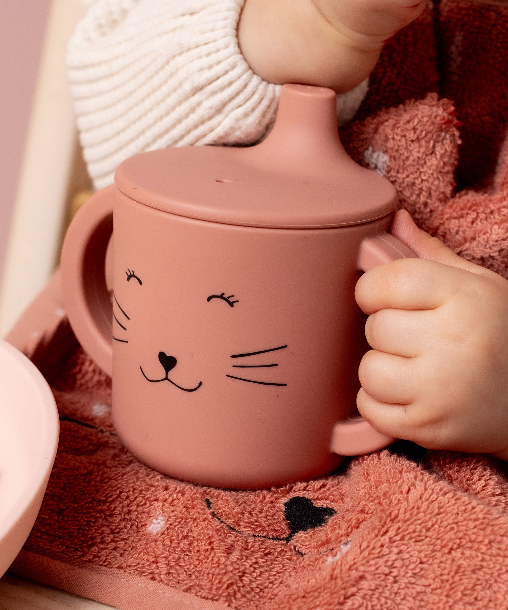 Child holding the handle of the Trixie Animal Friends Silicone Sippy Cup, pink, Mrs Cat.