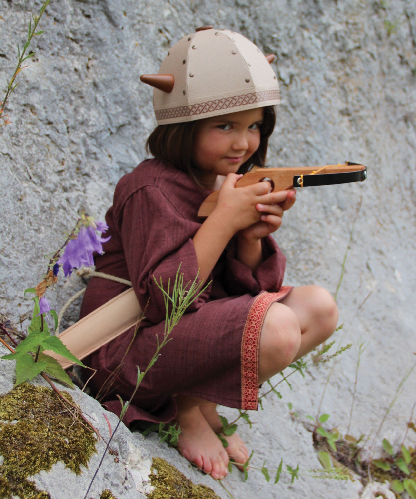 A child in full Viking costume including the Vah Viking Tunic, helmet and drinking horn. The child is playing with a cross bow.