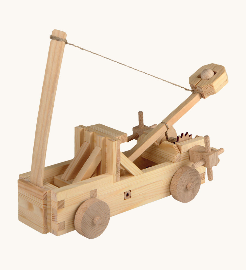 The Walachia Wooden Catapult made from wooden pieces, on a cream background. The image shows the catapult with a small wooden ball inside the movable arm, with a string attached to the arm and to a vertical piece of wood in front.