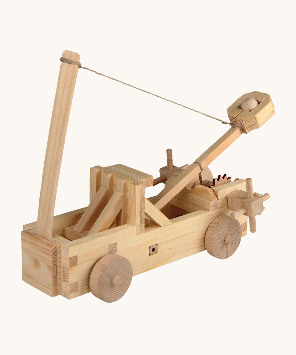 The Walachia Wooden Catapult made from wooden pieces, on a cream background. The image shows the catapult with a small wooden ball inside the movable arm, with a string attached to the arm and to a vertical piece of wood in front.