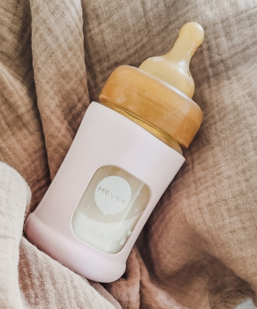 Hevea Glass Baby Bottle Wide Neck With Rubber Sleeve - 150ml in Sand on a taupe muslin blanket.