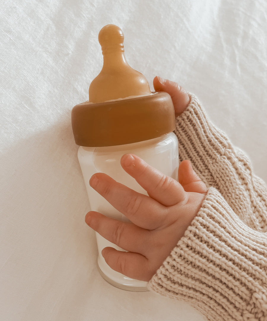 Baby wearing a cream  jumper with a Hevea Glass Baby Bottle