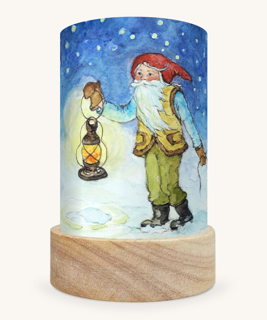 The Winter Gnome illustration by Eentje Van Margo sat in a Toverlux Magic Lantern base, on a cream background