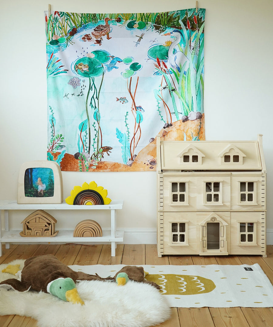 Wonderie Play Cloth - Down By The Pond on a play room wall, with toys and a dolls house underneath