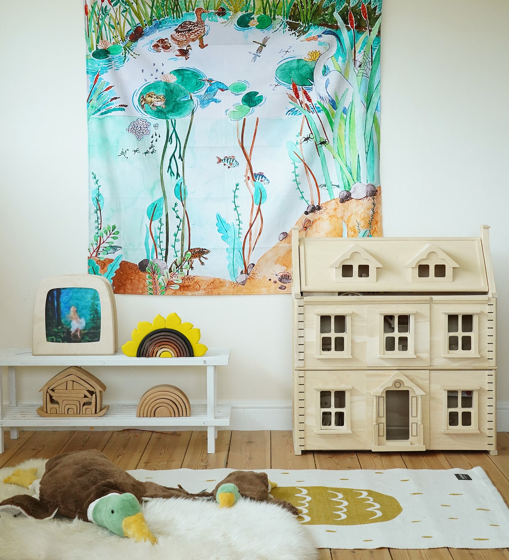 Wonderie Play Cloth - Down By The Pond on a play room wall, with toys and a dolls house underneath