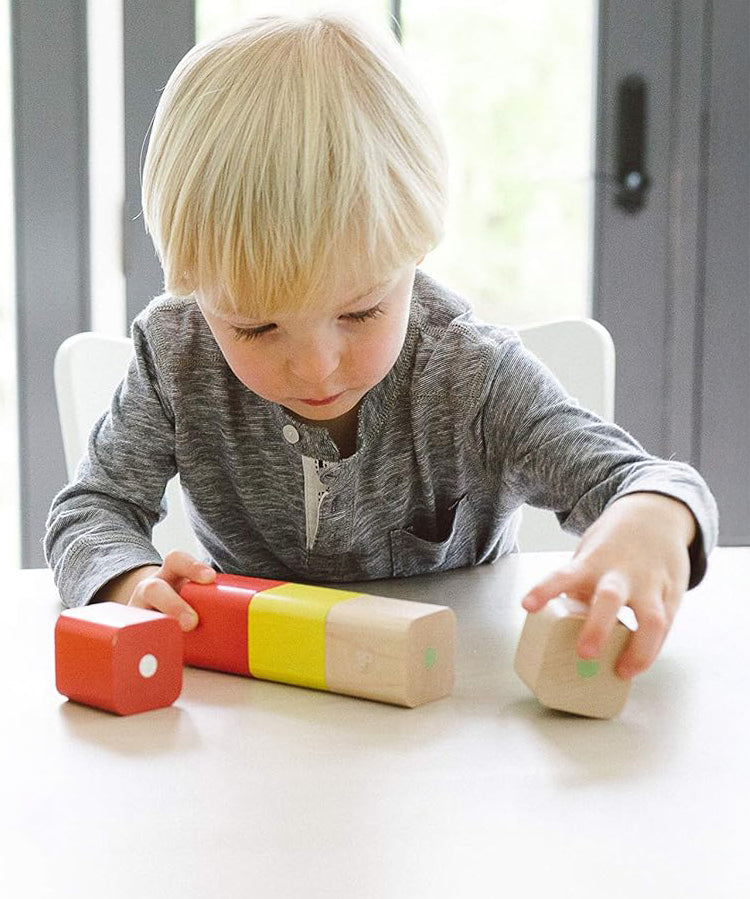 A child sat at a white table, playing with the Tegu Magnetic Wooden Blocks 