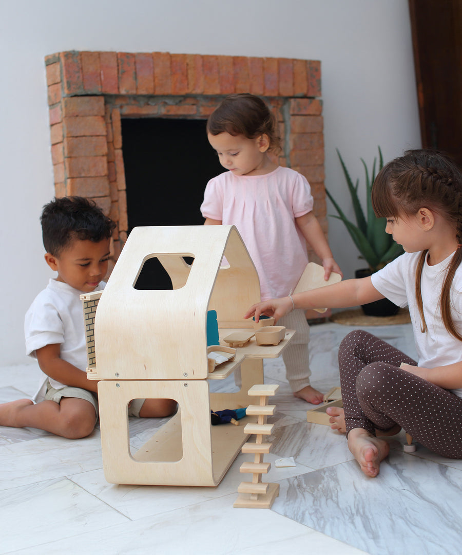 Three children playing with the PlanToys Contemporary Dolls House. There are wooden dolls and wooden furniture inside. 