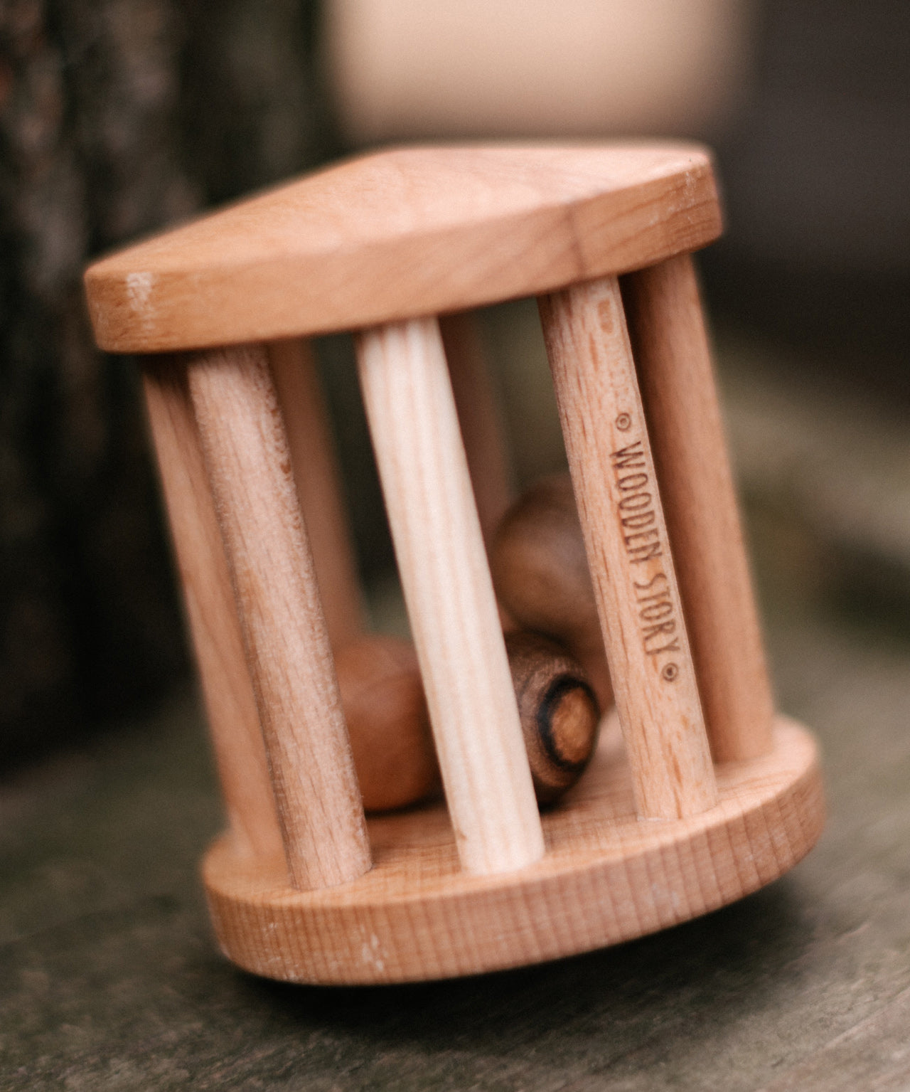 The Wooden Story Turtle Dove Rattle on its side, to show it can be twirled like a spinning top. The natural wood grain of the rattle and wooden balls shows through, and the words "Wooden Story" is etched onto the side of the rattle.