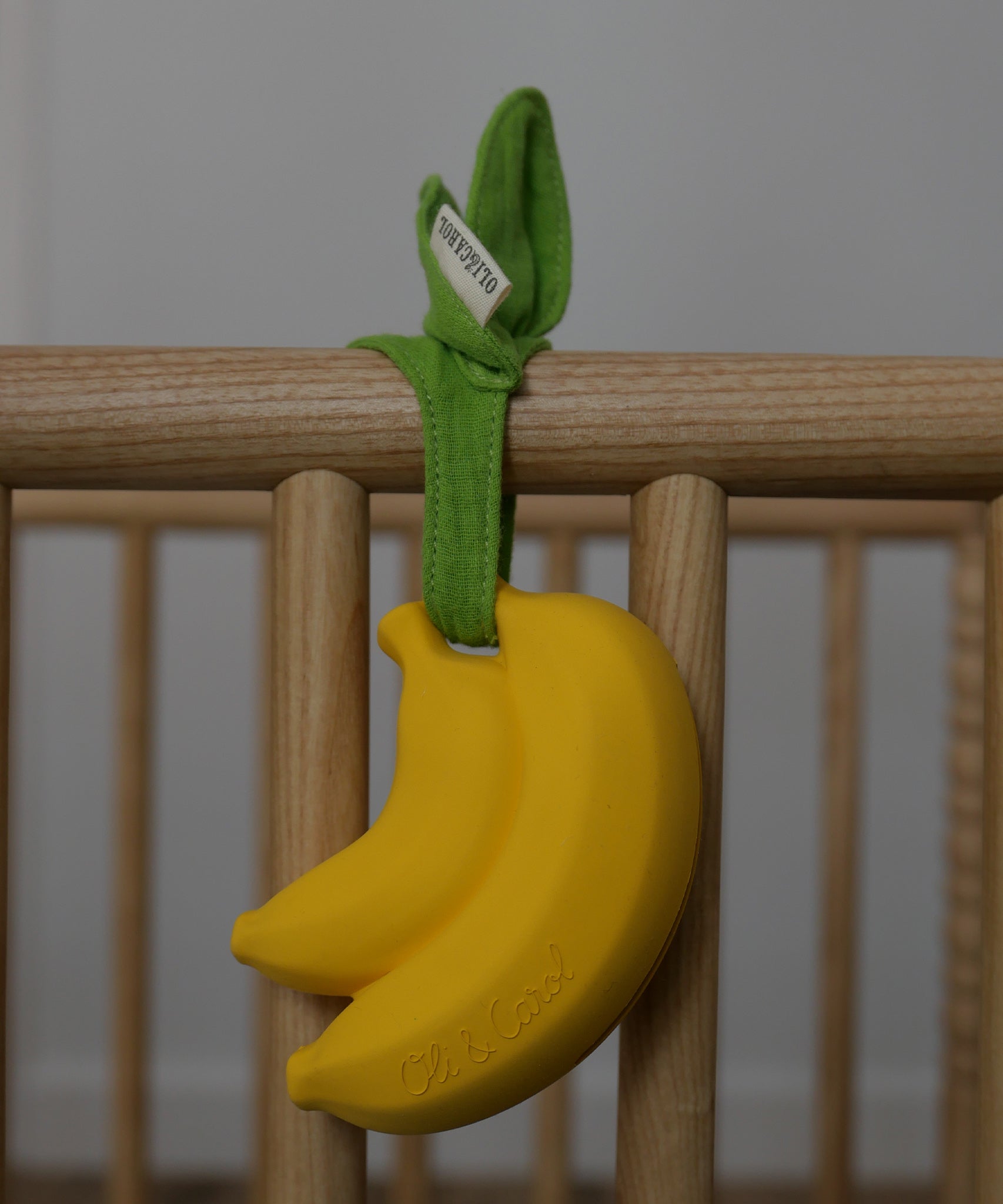 The Ana Banana Pacifier Holder is attached to the side of a wooden cot, with the muslin cloth leaves.