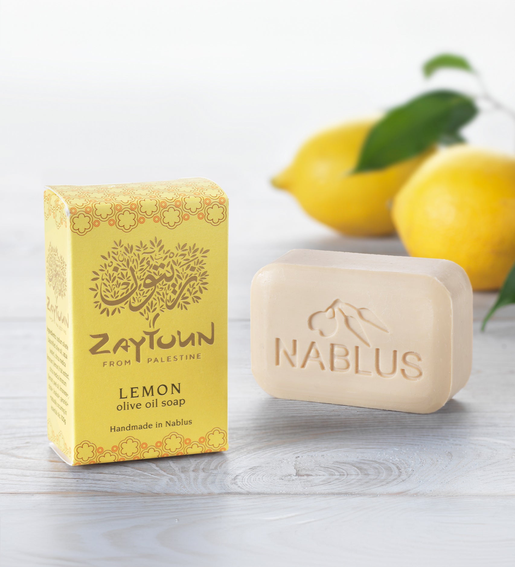 Zaytoun Pure Olive Oil Soap - Lemon 100g, next to its box and stood in front of a pair of lemons