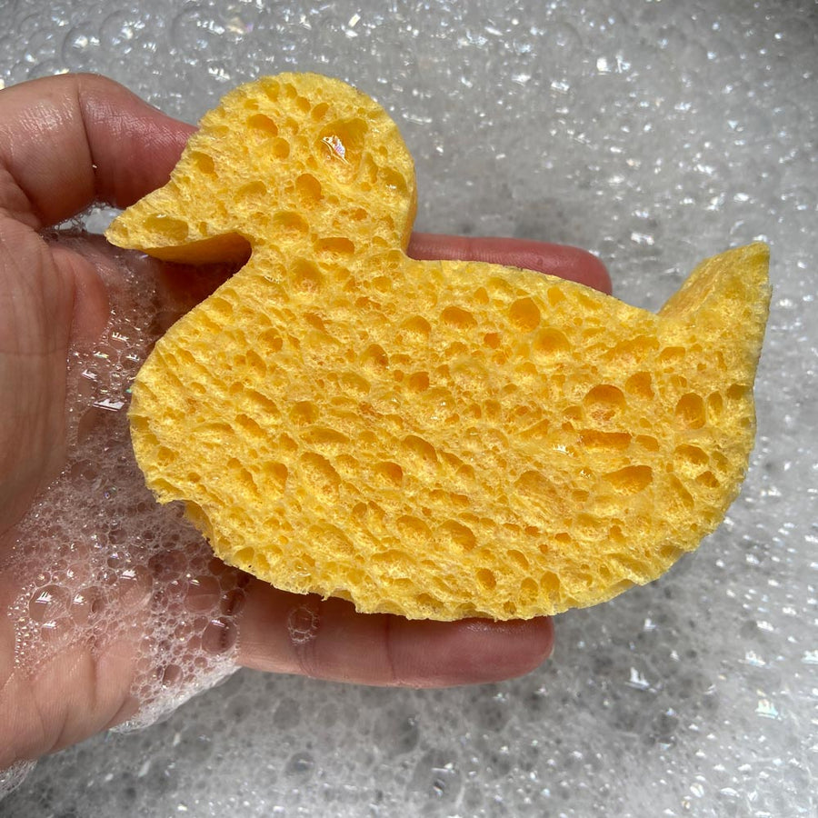 Close up of a hand holding A Slice of Green compostable cellulose duck sponge over some bubbles