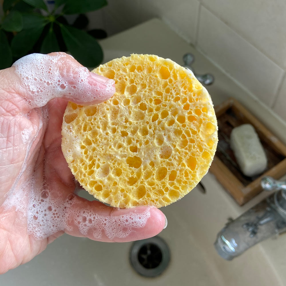 Close up of a hand holding A Slice of Green plastic-free exfoliating facial sponge