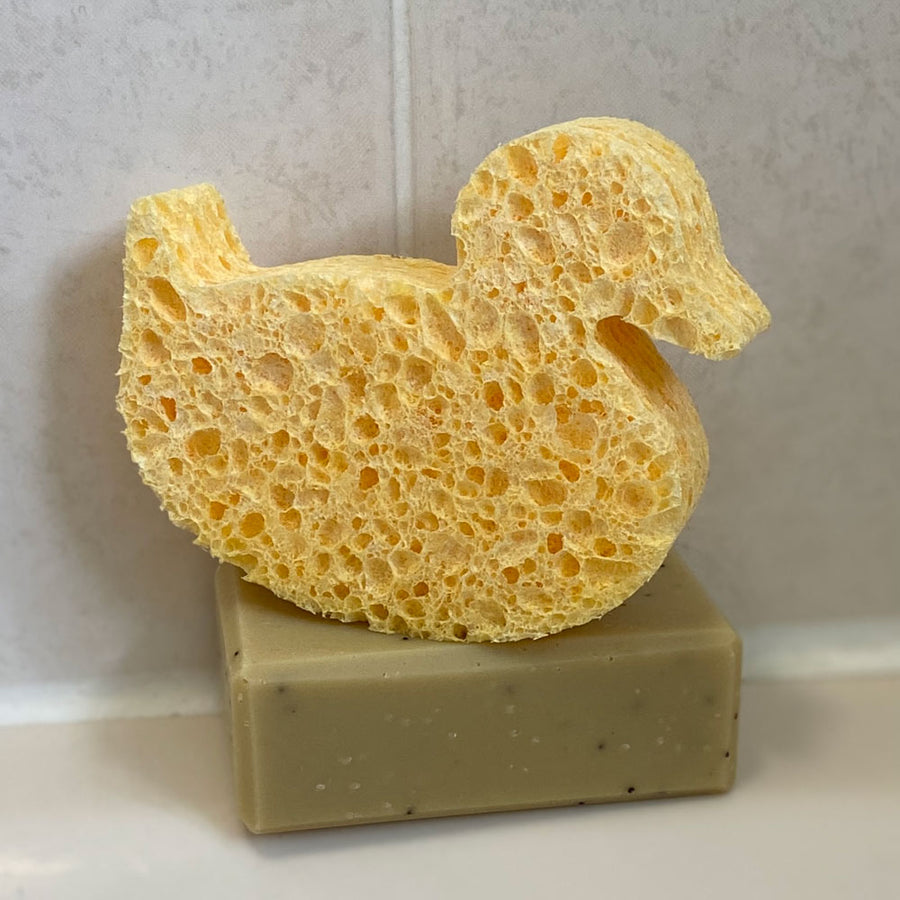 A Slice of Green plastic-free cellulose duck shape sponge on top of a green soap bar