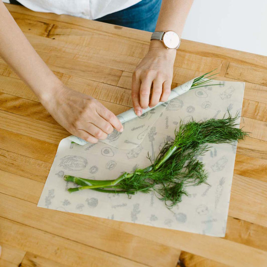 Hands rolling up some vegetables in the Abeego reusable plastic-free beeswax food wrap on a wooden worktop